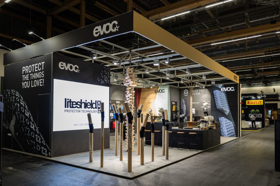Moderner Messestand mit dunklem Design, Produktvitrinen und Deckenbeleuchtung in Messehalle